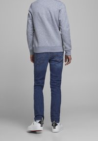 Šedá mikina se žebrovanými manžetami a lemem, v kombinaci s tmavě modrými džíny s viditelnými zadními kapsami, obutá s bílými teniskami.