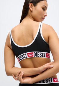 Sutiã desportivo preto com detalhes brancos, apresentando uma faixa larga na cintura com a marca "DIESEL" em vermelho e preto. Tecido macio e elástico, design com costas nadador.