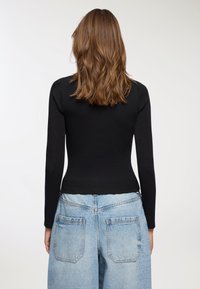 Czarny dopasowany top z długim rękawem i okrągłym dekoltem, zestawiony z jasnoniebieskimi, luźnymi dżinsami o wysokim stanie z tylnymi kieszeniami.