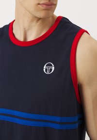 Mornarica brezrokaven majica z rdečimi obrobami; ima dve vodoravni modri črti na sprednji strani in belo krožno logotip na prsih.