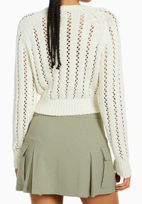 Cremfarbener gestrickter Pullover mit Lochmuster, gerippten Bündchen und Saum, kombiniert mit einem olivgrünen, plissierten Rock mit Seitentaschen.