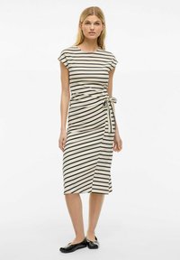 Pasiasta sukienka midi w kremowo-czarnym kolorze; miękka tkanina, dopasowana talia z wiązaniem po boku, krótkie rękawy i rozcięcie na hemie dla swobody ruchów.