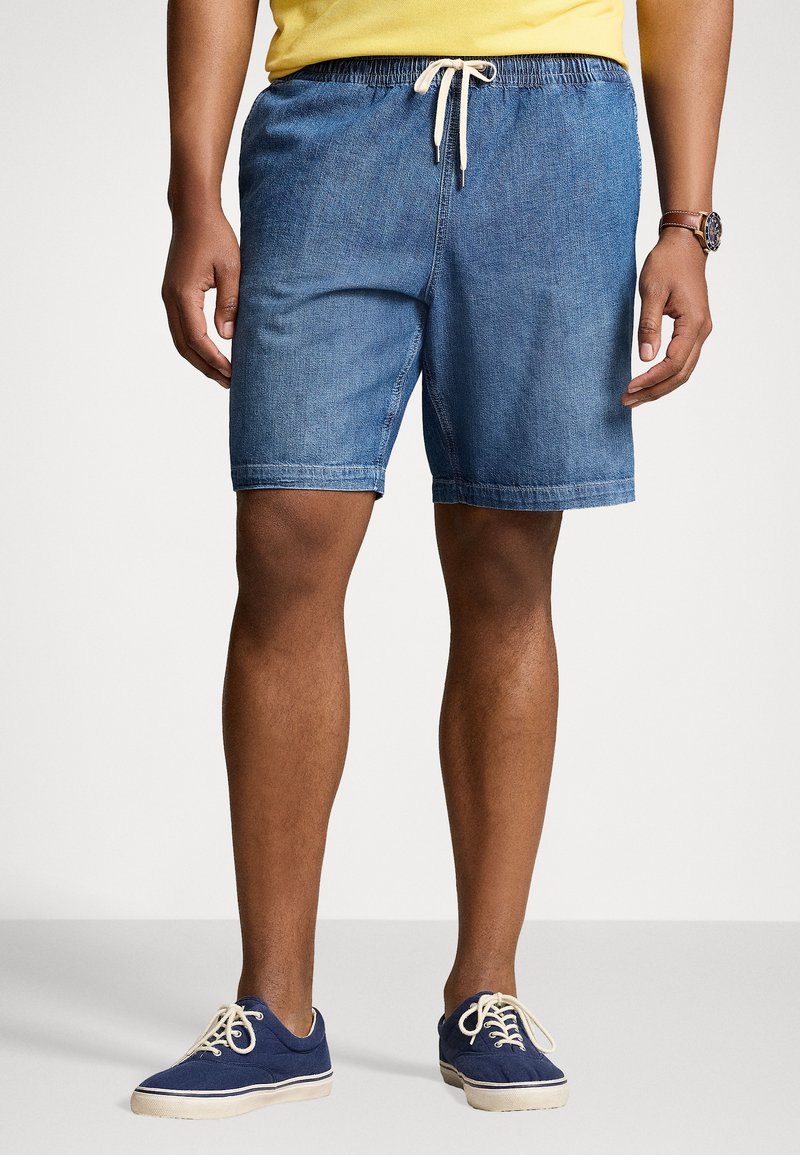 Shorts en denim bleu avec une taille élastique et un cordon de serrage. Les shorts ont des poches latérales et une coupe décontractée, associés à des chaussures navy.