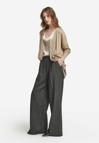 Beige Cardigan mit fließender und weicher Textur, kombiniert mit grauen, weit geschnittenen und strukturierten Hosen. Beide Teile haben einen entspannten Schnitt und ein reduziertes Design.