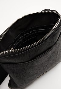 Svart texturerad läderaxelväska med silverfärgad dragkedja, med ett huvudfack och flera inre fickor för organisering.