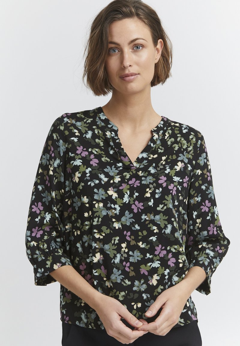 Blomstret bluse med sort bund og grønne, lilla og blå mønstre, v-hals og 3/4 ærmer, lavet af letvægtsmateriale.
