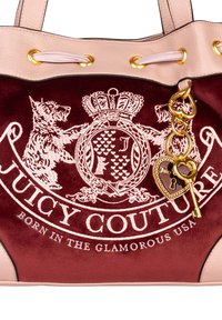 Borsa tote in velluto bordeaux con finiture in pelle rosa chiaro, hardware dorato e un charm con design a cuore e chiave. Logo Juicy Couture stampato in modo prominente.