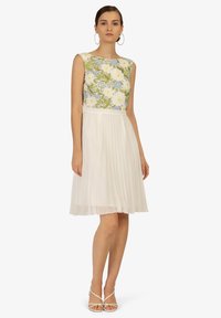 Robe florale avec un corsage sans manches arborant un motif floral vert, bleu et blanc ; jupe blanche fluide et plissée ; longueur sous le genou.