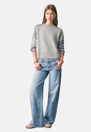 Suéter de punto gris claro con dobladillo acanalado y corte relajado, combinado con jeans de pierna ancha azul claro y zapatos planos rosas.