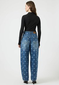 Džíny s širokými nohavicemi z denimu s modrým puntíkovaným vzorem, vybavené pěti kapsami a hnědou zadní nášivkou, kombinované s černým topem s dlouhým rukávem.