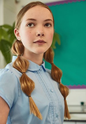 Lichtblauwe kortekragen shirt met een knoopsluiting en decoratieve steken, gedragen door een meisje met twee gebonden, golvende blonde vlechten.