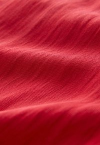 Zbliżenie czerwonej tkaniny o delikatnej żebrowanej teksturze i łagodnych fałdach tworzących miękkie cienie i refleksy światła.