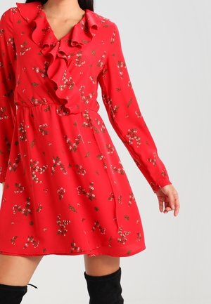 Vestido rojo con flores, de mangas largas y con un escote rizado. La tela es ligera y suave, con pequeños patrones de flores en blanco y verde.
