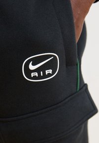 Fekete sportnadrágon jól látható fehér Nike logó található, az "AIR" felirattal. Az anyag sima, texturált felülettel és látható varrásokkal rendelkezik.