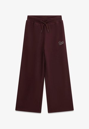 Pantalon de survêtement marron foncé à jambes larges avec taille élastique et cordon, présentant un petit logo blanc "Guess EST. 1981" sur la cuisse gauche.