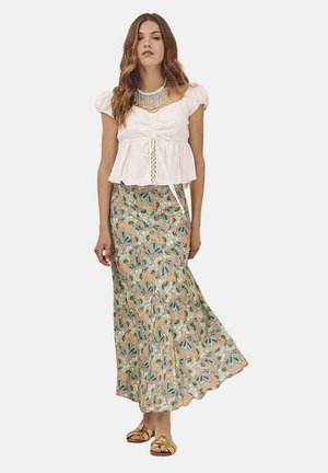Blusa blanca con mangas abullonadas y detalle de lazo en la cintura, combinada con una falda larga y fluida con patrones florales en turquesa y naranja. Sandalias doradas.