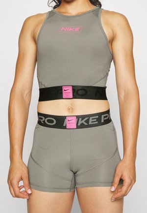 Sportovní osoba nosí šedý sportovní crop top Nike Pro a odpovídající šortky s černými pásky v pase, na kterých jsou růžové štítky Nike Pro.