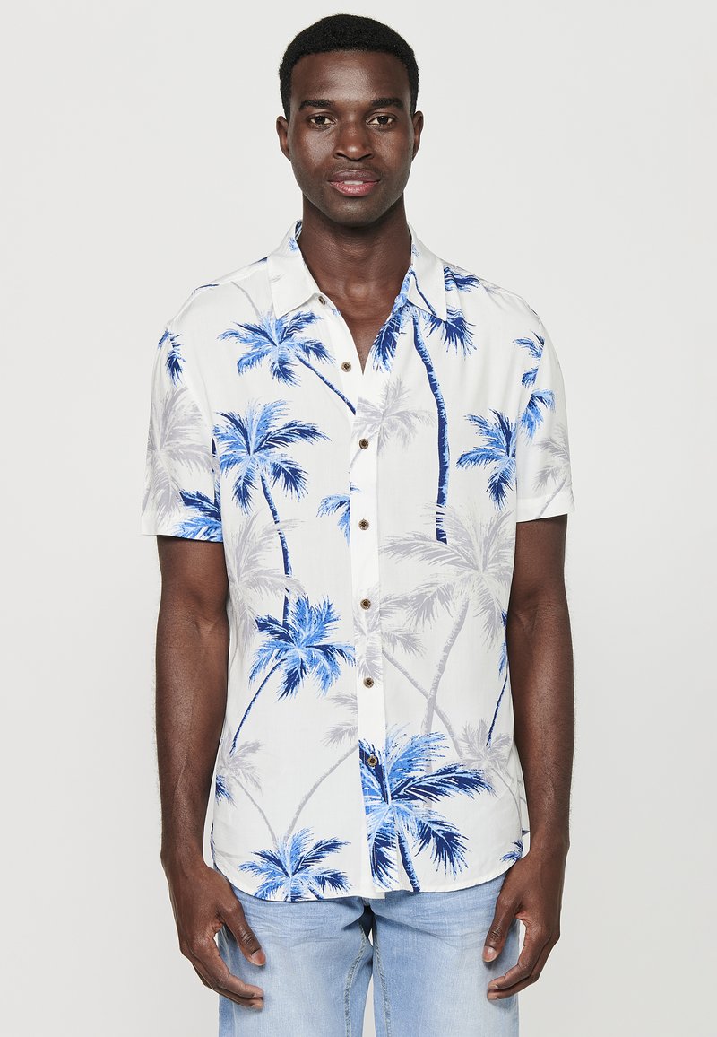 Camicia a maniche corte bianca con stampa di palme blu. Presenta una chiusura con bottoni e una vestibilità rilassata. Tessuto leggero con una texture liscia.