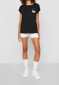 Svart bomull t-shirt med uppvikta ärmar, med ett hjärt- och irländskt flaggmotiv på bröstet. Bärs med vita shorts och sneakers.