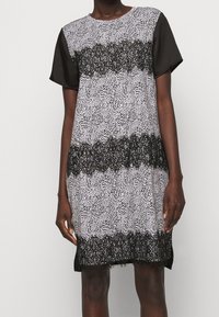 Černobílé šaty s krátkým rukávem, které mají skvrnítý vzor a krajkové detaily na lemování a v střední části. Hladká textura, volný střih.