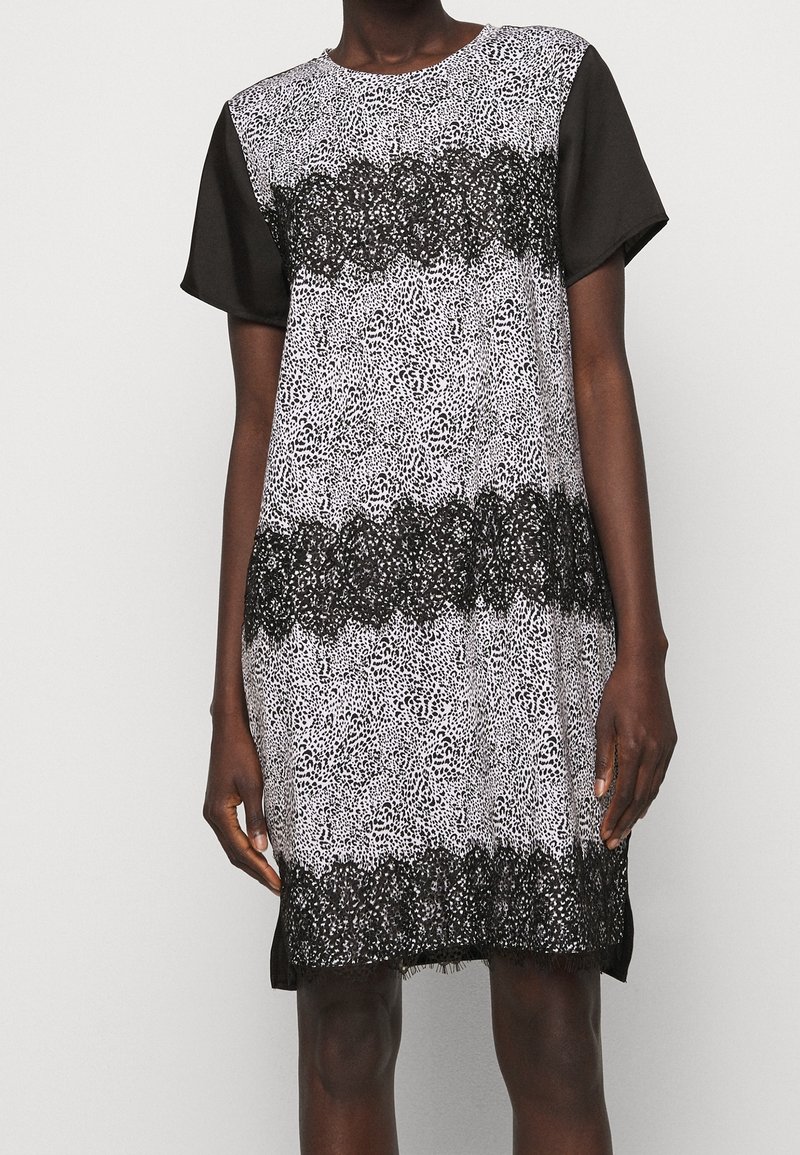 Černobílé šaty s krátkým rukávem, které mají skvrnítý vzor a krajkové detaily na lemování a v střední části. Hladká textura, volný střih.