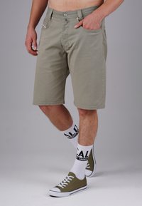 Hellgrüne Baumwollshorts mit geradem Schnitt, Front- und Gesäßtaschen sowie Metallbeschlägen; kombiniert mit weißen Socken und grünen Sneakern.