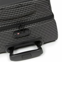 Bolsa a cuadros en blanco y negro con un asa retráctil, cierre de cremallera y una etiqueta de marca. Material duradero con una forma estructurada.