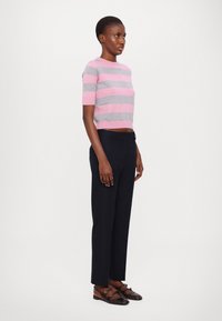 Rutet kortermet topp i rosa og grått, kombinert med mørk marineblå dressbukser og brune flate sko. Enkel, tettsittende design, strukturert strikket stoff.