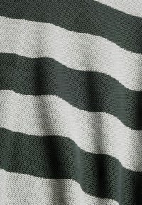 Gros plan d’un tissu avec des larges rayures horizontales alternées vert foncé et blanc tricotées, montrant un motif texturé et de légers plis.