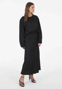 Schwarzes Zweiteiler-Outfit, das aus einem langärmeligen Oberteil mit Rundhalsausschnitt und einem high-waisted, fließenden Rock besteht. Die Textur ist glatt, der Stoff wirkt leicht.