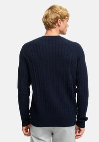 Granatowy sweter w splot kablowy z prążkowanymi mankietami i dołem, charakteryzujący się teksturowanym wzorem i rękawami raglanowymi. Wykonany z miękkiego, ciepłego materiału.