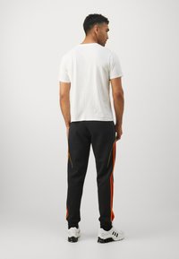 Black joggers with orange side stripes, paired with a white crew neck t-shirt. Model shown from the back, wearing white sneakers.