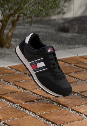 Zwarte sneaker met witte accenten, met Tommy Jeans branding en gekleurde strepen. Materiaal lijkt glad, met een gestructureerde zool.