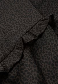 Tela negra con un sutil estampado de leopardo. El borde incluye un detalle de volantes a lo largo de la costura, que añade textura y dimensión.