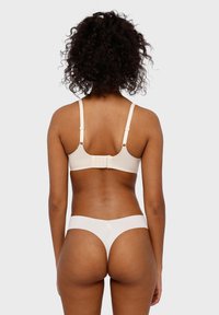 Reggiseno beige con spalline regolabili e chiusura a gancio. Tanga bianco senza cuciture in abbinamento con dettaglio logo. Texture liscia, design semplice.