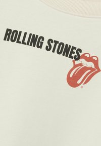 Kremowy sweatshirt z czarnym napisem "ROLLING STONES" oraz czerwonym logo języka. Posiada ribbowany dekolt i gładką teksturę.