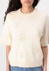 Crème korte mouwen trui met geborduurde bloemen, geribbelde halslijn en boorden, zachte textuur en een relaxte pasvorm.