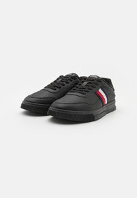 Czarne sneakersy z teksturowanej skóry, zdobione perforowanymi detalami, z grubą gumową podeszwą i bocznym paskiem w kolorze czerwonym, białym i niebieskim.