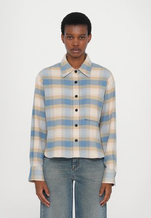 Cropped, long-sleeve flannel shirt in blue, beige, and pink plaid. Features black buttons and a single chest pocket, made of soft fabric.