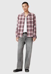 Punase ja halli ruudulise flanellsärgi kaks rinnataskut, nööbitav disain ja all valge T-särk, mida on kombineeritud helehallide teksadega.