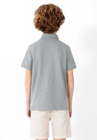 Polo gris à manches courtes avec col, fabriqué en matériau doux. La vue de dos montre une coupe décontractée, associée à un short beige clair.