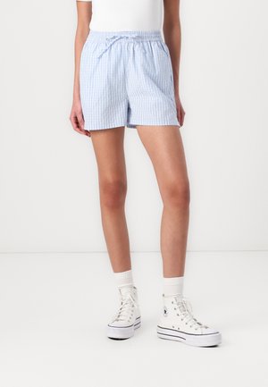 Persona con pantalones cortos a rayas azul claro y blanco con cintura elástica y cordón, calcetines blancos y zapatillas blancas altas.