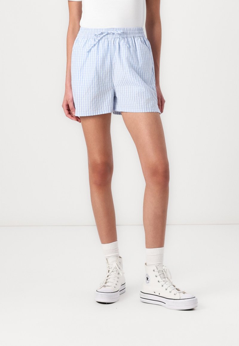 Personne portant un short rayé bleu clair et blanc avec taille élastique et cordon, chaussettes blanches et baskets blanches montantes.