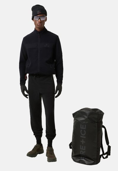 Black zip-up fleece jacket with matching joggers, gloves, and beanie, paired with a black roll-top backpack featuring a logo print.