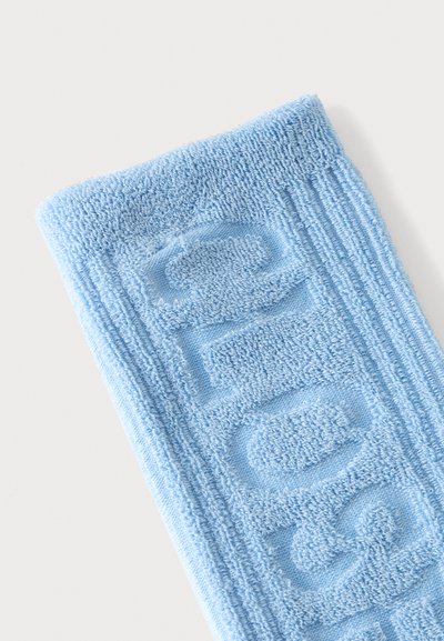 Tissu tricoté bleu clair avec des lettres en relief texturées et des bords côtelés sur un fond clair uni.