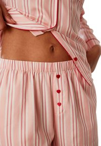 Rosa randig pyjamaset med röda detaljer, knappstängning och elastisk midja i ett texturerat tyg. Vertikala ränder genom hela.