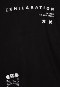Schwarzes Baumwoll-T-Shirt mit auffälligem weißen Text und Phrasen sowie einer Skateboard-Grafik. Weiche Textur, lässige Passform, ungezwungene Gestaltung.