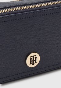 Portafoglio in pelle blu navy con superficie testurizzata, cerniera dorata e un elemento metallico rotondo con logo impresso in nero.