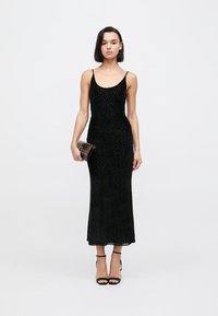 Μαύρο, αμάνικο μάξι φόρεμα με εφαρμοστή σιλουέτα, διακοσμημένο με υφή σε σχέδιο λεοπάρδαλης. Συνδυασμένο με ένα μικρό καφέ τσαντάκι και μαύρα τακούνια.