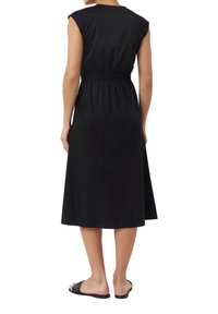 Czarna midi sukienka z krótkimi rękawami, marszczonym stanem, gładkiego materiału i luźnym kroju; noszona z czarnymi płaskimi sandałami.